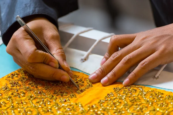 Hands sew fabric to make a costume for Thai puppet