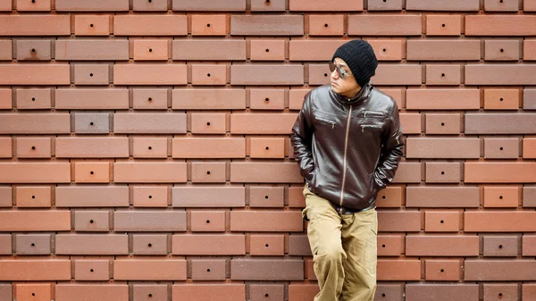 An Asian Man in a Brown Jacket Leans  Against the Wall