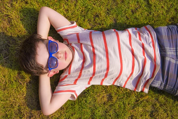 Boywith sunglasses sunbathing on the grass in the summertime