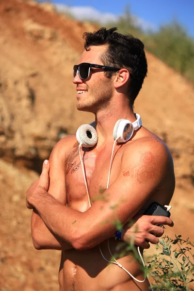 Happy naked muscular young man standing in the desert smiling and embracing herself. Demonstrates sports figure, muscles.