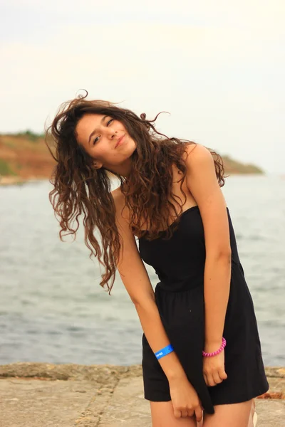 Beautiful slim brunette girl model posing in fashion dress by the sea, outdoor portrait