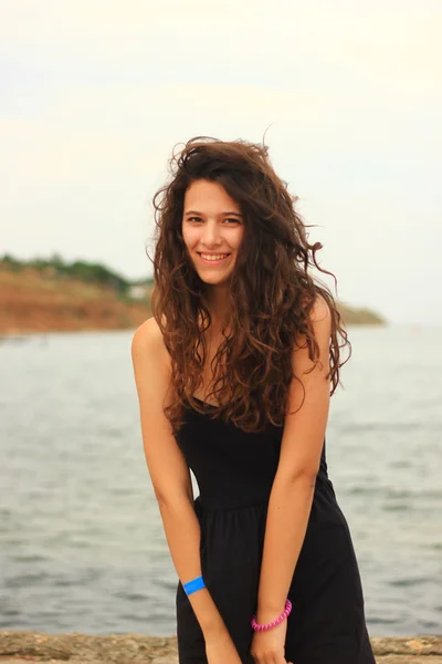 Beautiful slim brunette girl model posing in fashion dress by the sea, outdoor portrait. Natural look.