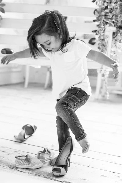 Little girl in white T-shirt and jeans playing and trying on her mother\'s high heels