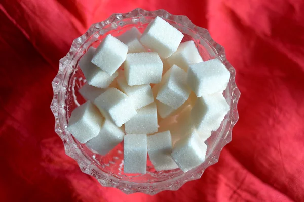 Pieces of cube sugar in crystal sugar bowl on a  red background