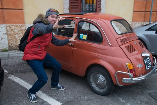 Young guy doing selphy next to a small car in Italy