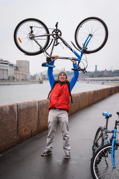 A young man picks up a bicycle over his head during a trip to the city in the fall after the rain
