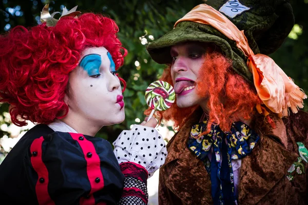 Young woman and man in the image of the Hatter and the Red Queen from the fairy tale about Alice eat huge candy