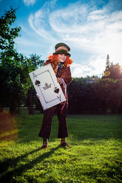 Young man in the image of the Hatter from the fairy tale about Alice with a huge playing card