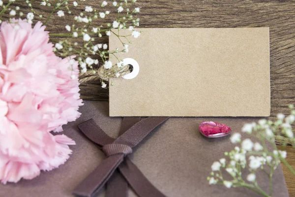 Blank paper tag with carnation flower on wooden background