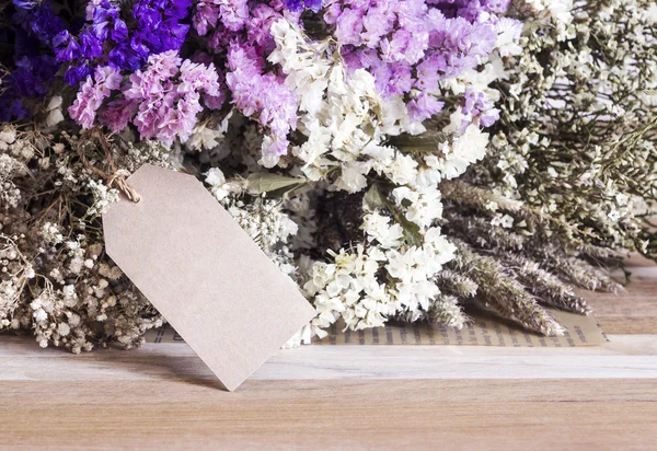 Bouquet of dried flowers with blank paper tag on the wooden tabl