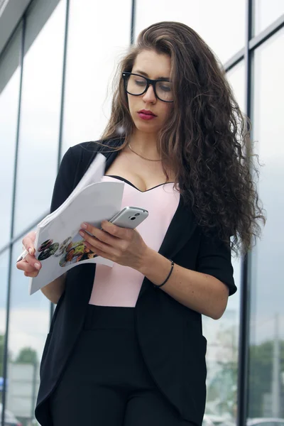 Successful business woman or businesswoman holding a magazine and talking on a cellphone , standing in front of his office.