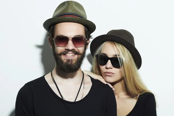 Beautiful happy couple in hat wearing trendy glasses together. Hipster boy and girl. Bearded young man and blonde in sunglasses