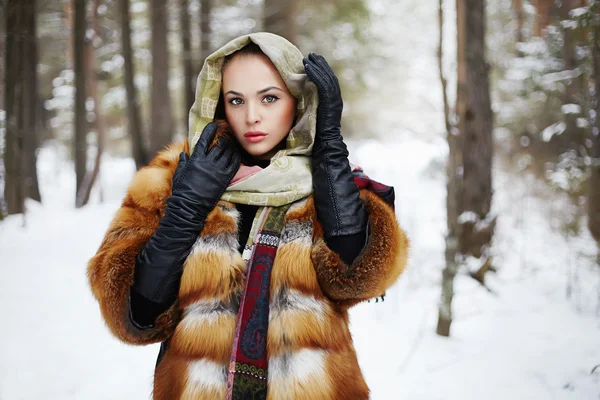 Beauty model in winter forest. beautiful young Woman in fashionable Fur Coat,leather gloves and scarf