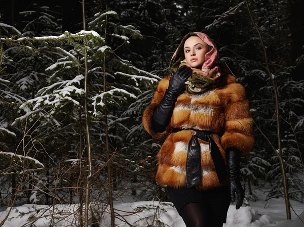 Beautiful young Woman in fashionable Fur Coat and scarf at night in winter forest