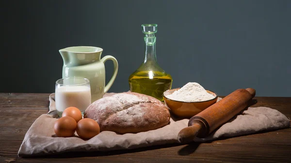 Still life photo of bread and flour with milk and eggs at the wo