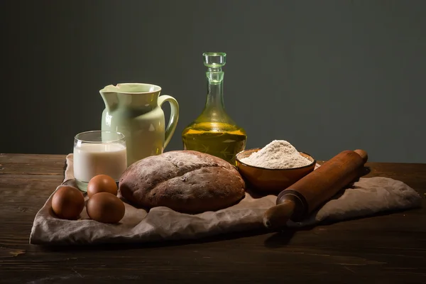 Still life photo of bread and flour with milk and eggs at the wo