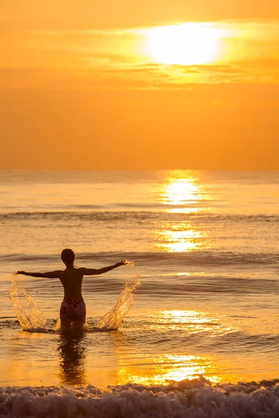 Silhouette of woman that plays with water at the sea