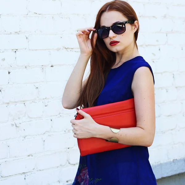 Fashion young woman wearing sunglasses, blue top with red lutch