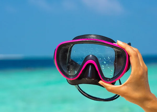 Hands holding scuba mask on tropical beach