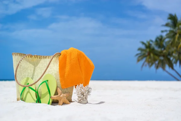 Summer beach bag with starfish,towel,sung lasses and flip flops on sandy beach