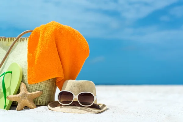 Summer beach bag with starfish,towel,sung lasses and flip flops on sandy beach