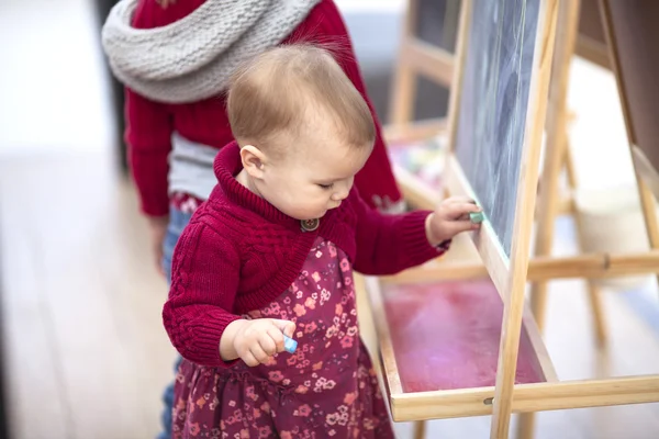 Baby girl draws chalk on  blackboard in children's area  shoppin