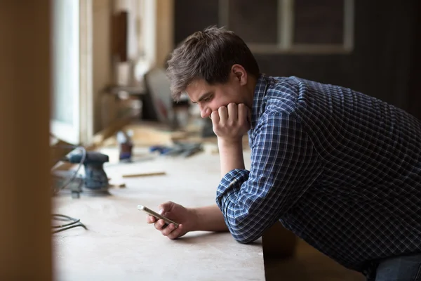 Craftsman leaning against  work area in his workshop using his c