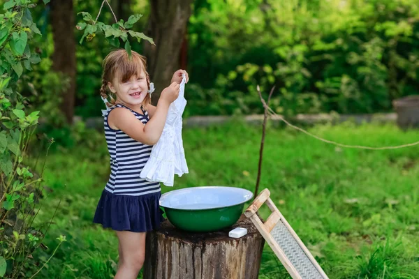 Little helper girl washes clothes in a basin outdoors