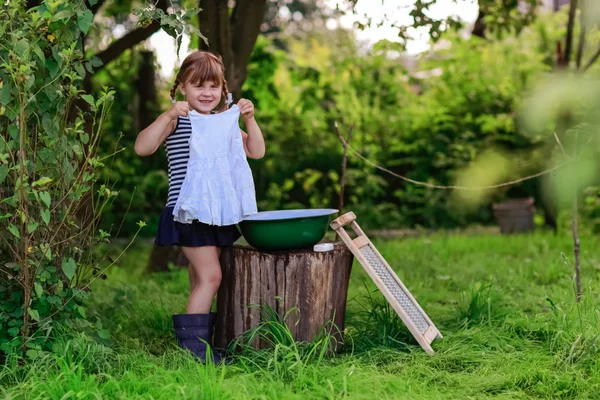Little helper girl washes clothes in a basin outdoors