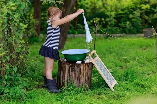 Little helper girl washes clothes in a basin outdoors