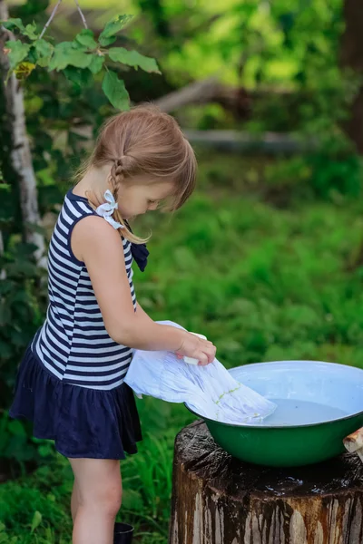 Little helper girl washes clothes in a basin outdoors