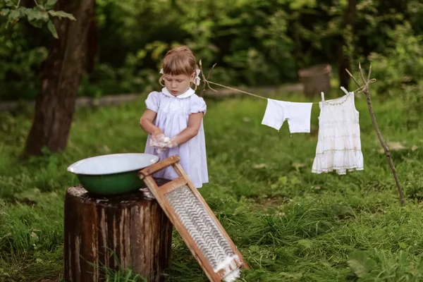 Little helper girl washes clothes   in a basin outside