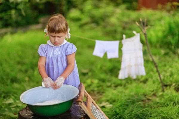 Little helper girl washes clothes   in a basin outside