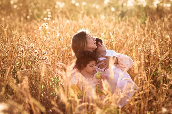 Mother hugging her son and daughter in a wheat field