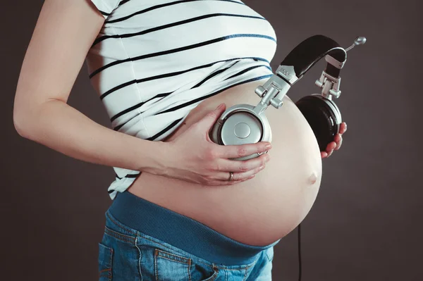 Belly of a pregnant woman. Listen to music with headphones.