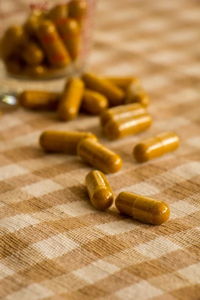 Glass cup of herbal medicine capsules on cotton.