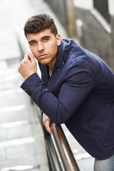 Handsome young man with blue eyes posing near a wall