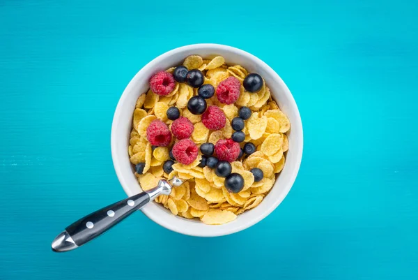 Cornflakes cereal with raspberries and bilberries and black currant in a white bowl