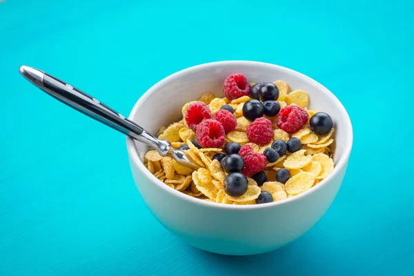 Cornflakes cereal with raspberries and bilberries and black currant in a white bowl