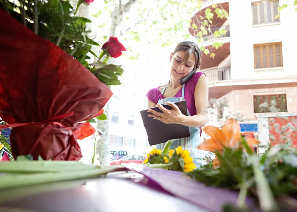 Florist woman using the phone with a clipbard in her store