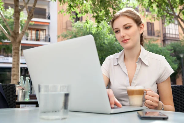 Business woman drinking a beverage and using laptop computer