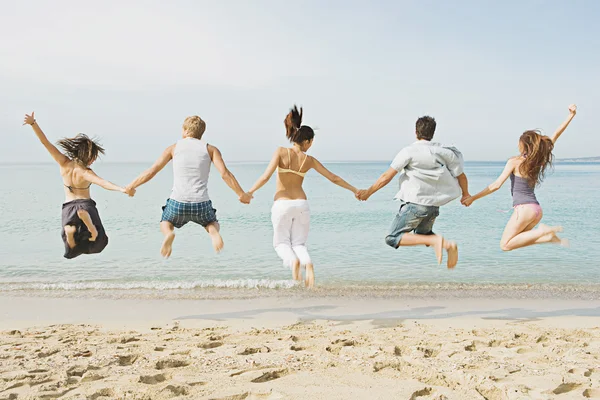 Friends holding hands and jumping on the beach