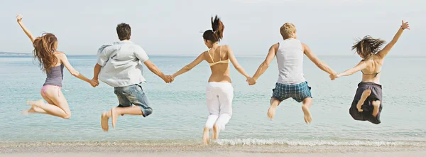 Friends holding hands and jumping on the beach