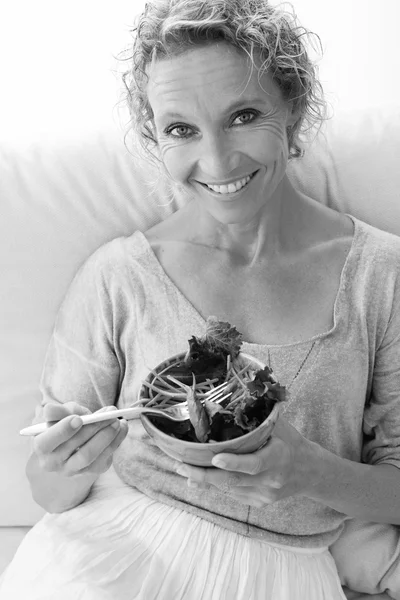 Woman eating a salad on a couch at home