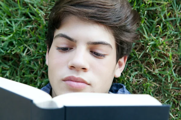 Student boy reading a book on grass