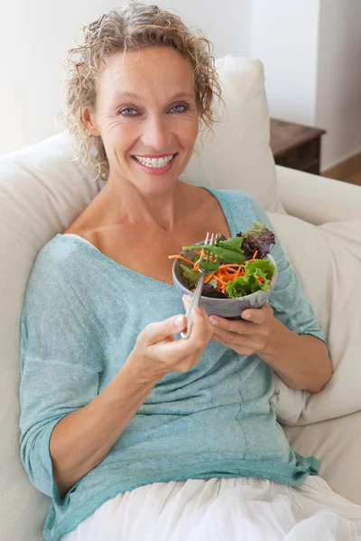 Woman eating a salad on a couch at home