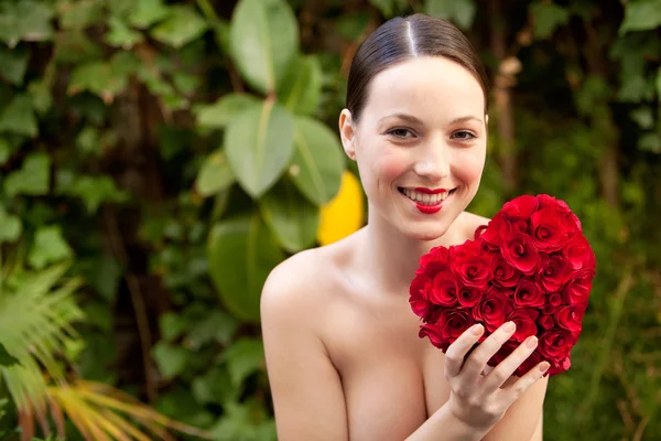 Nude girl holding a red roses heart in a garden