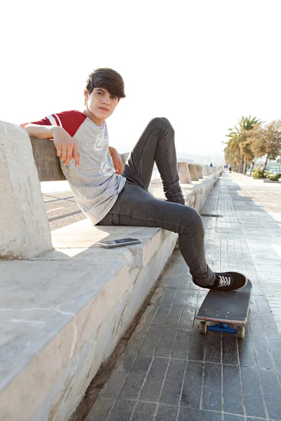Boy sitting on a bench with his skateboard and his smartphone