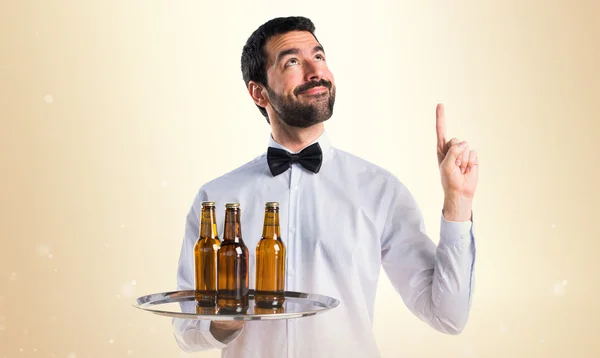 Waiter with beer bottles on the tray pointing up