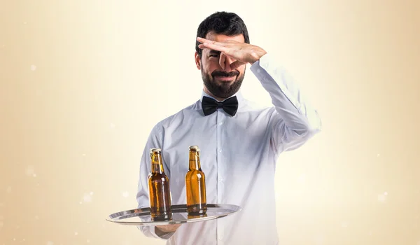 Waiter with beer bottles on the tray making smelling bad gesture